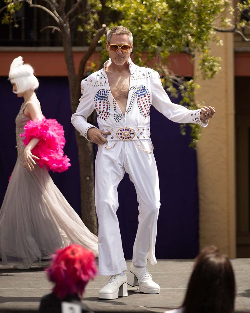 model playing air guitar in platform shoes and a white jumpsuit with white, red, white, and blue spangles