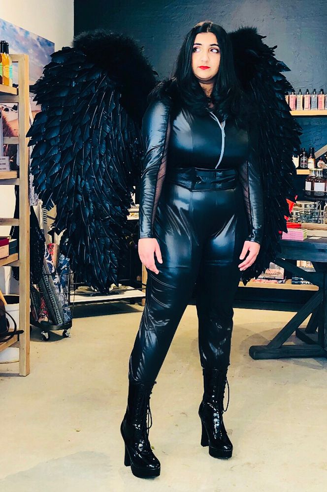 plus-size model in front of store display in black pleather unitard, black boots, and large black wings made from real feathers