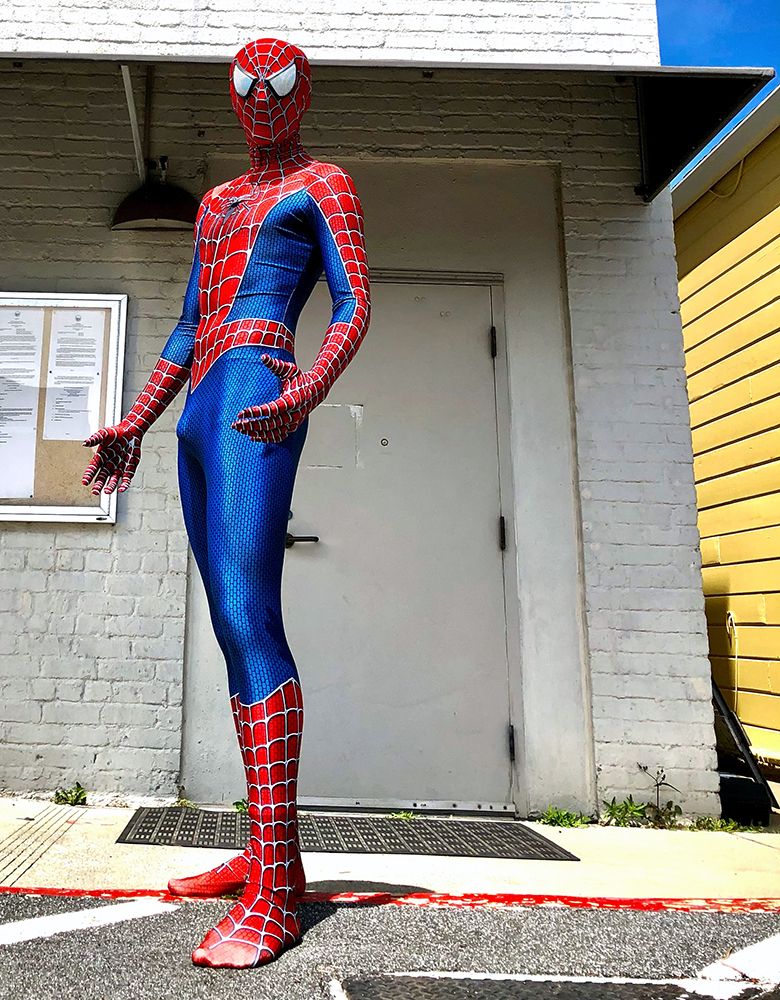 model in form-fitting spiderman costume in front of white brick wall