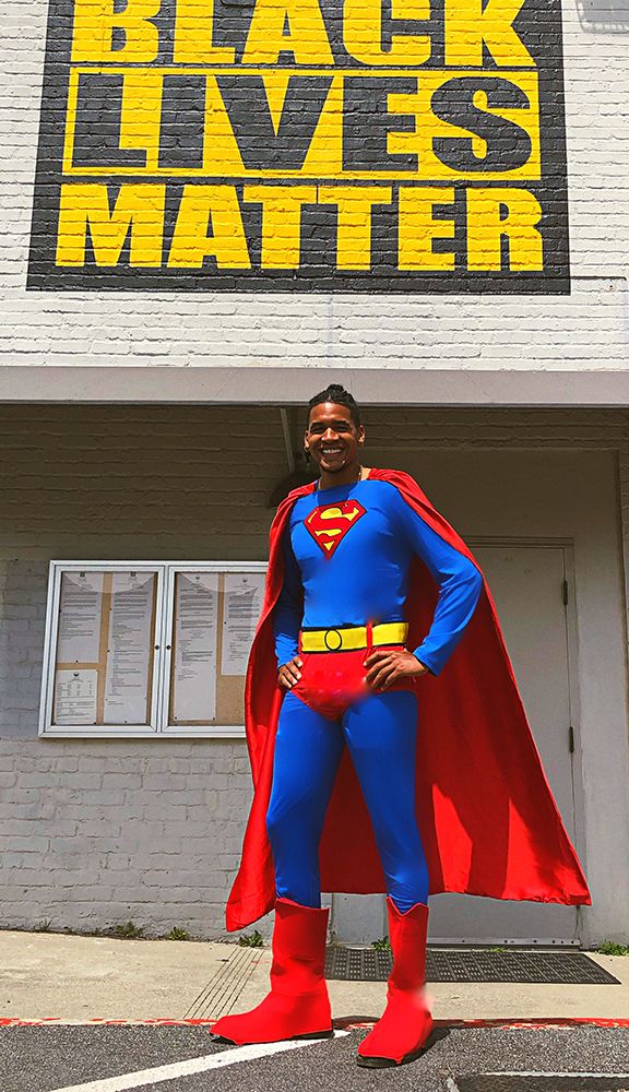 smiling man in superman costume in front of black lives matter mural