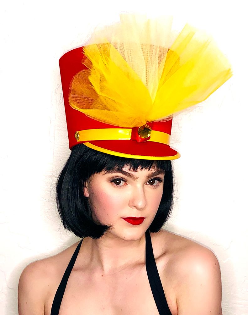 model in a black bob wig and red bandleader hat with yellow trim