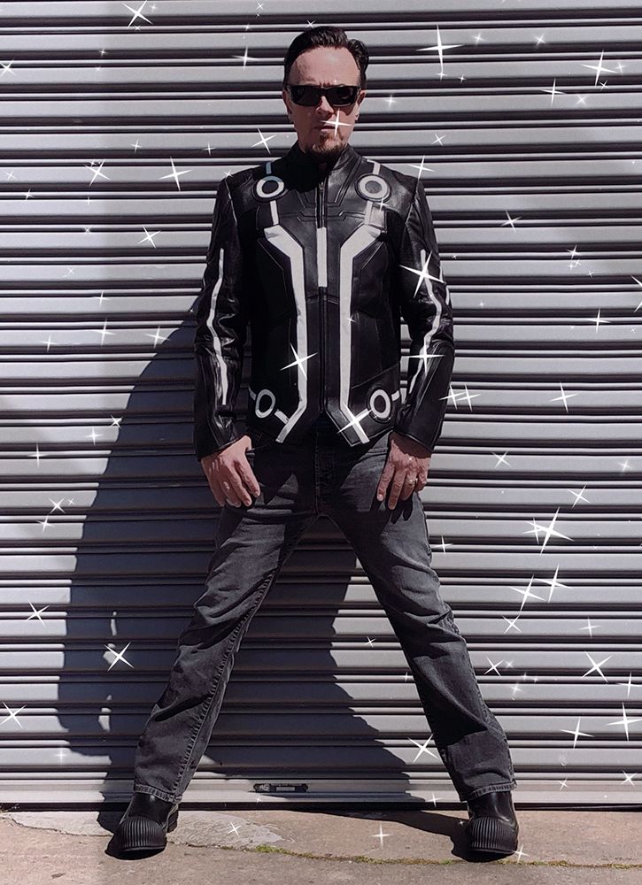model in black and silver tron leather jacket and dark glasses, standing in front of industrial garage door